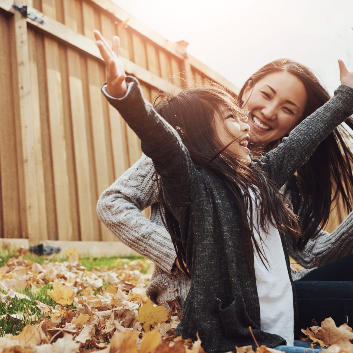 Seorang ibu tersenyum bahagia sambil bermain daun bersama anak perempuannya, menggambarkan kehangatan dan koneksi emosional yang terjalin melalui Tes Mind Modes™ Keluarga.