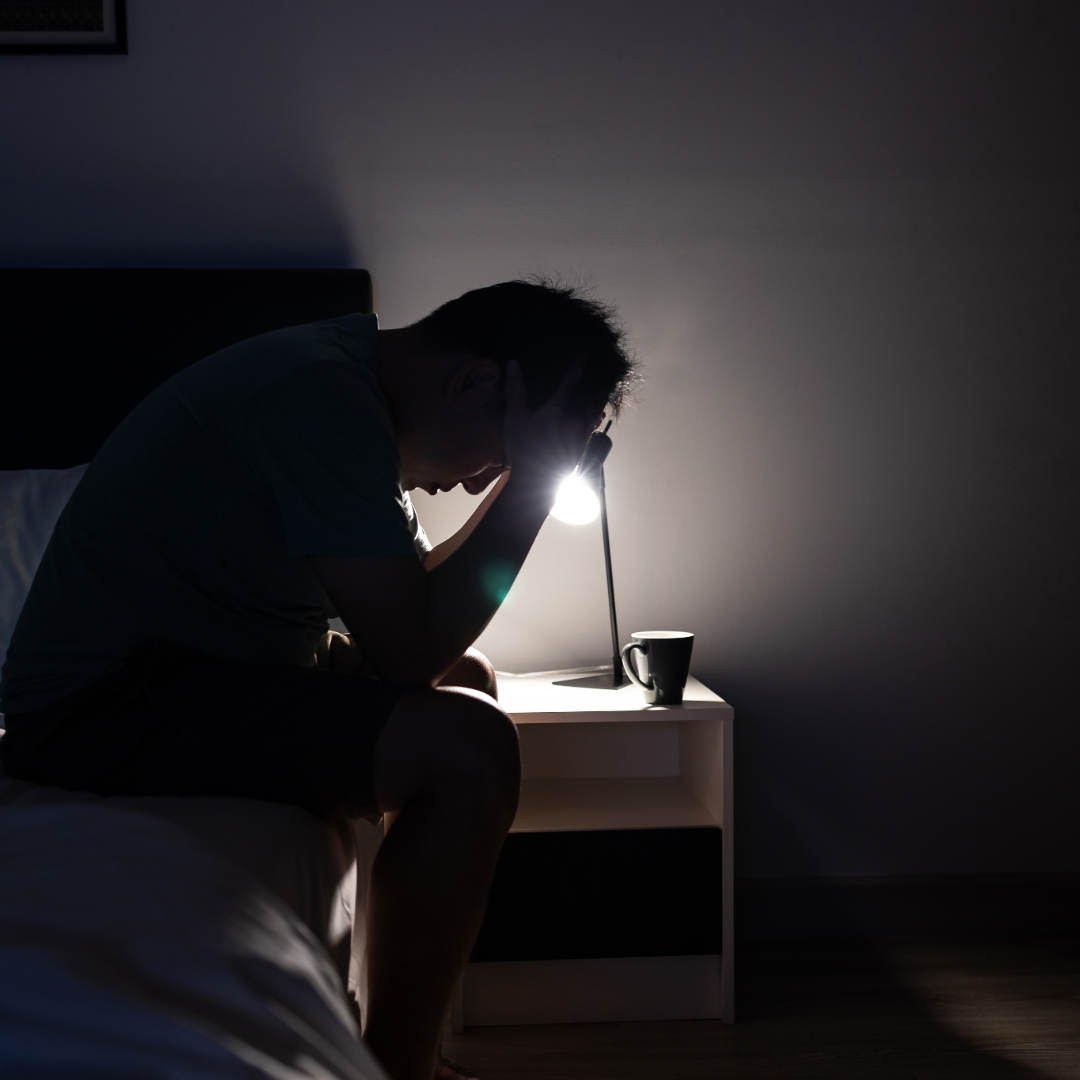 Pria duduk sendirian di kamar dengan ekspresi stres, menggambarkan tekanan emosional dan kelelahan mental.